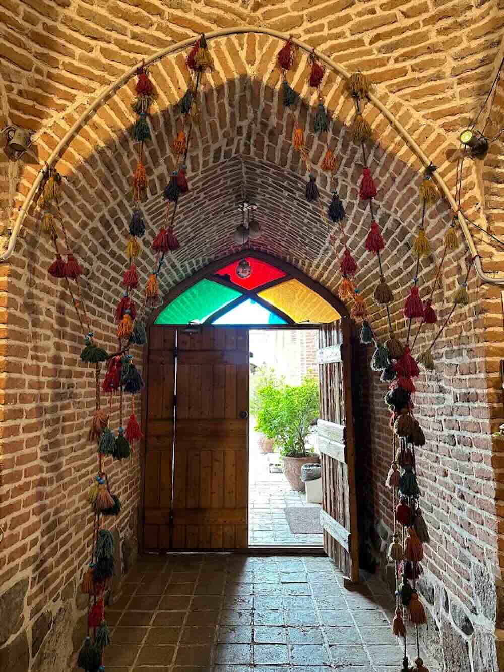 ورودی آجری کاروانسرای تاریخی ایران با طاق سنتی، در چوبی و تزئینات رنگارنگ دستبافت